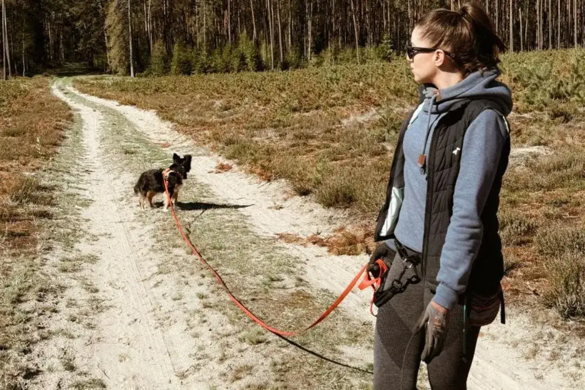 Kobieta z psem na smyczy na leśnej ścieżce. Warto mieć przy sobie smakołyki i woreczki na odchody, gdy zastanawiasz się, co wziąć na spacer z psem.